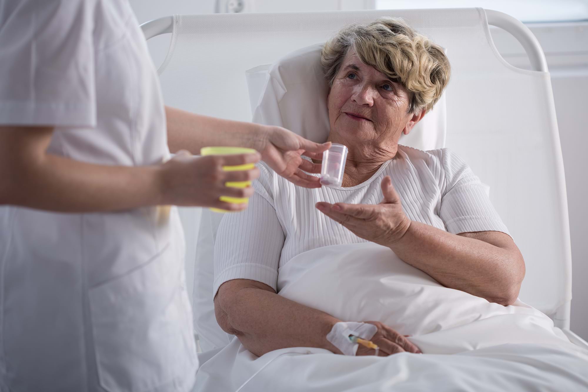 A woman being handed medication in a hospital bed
